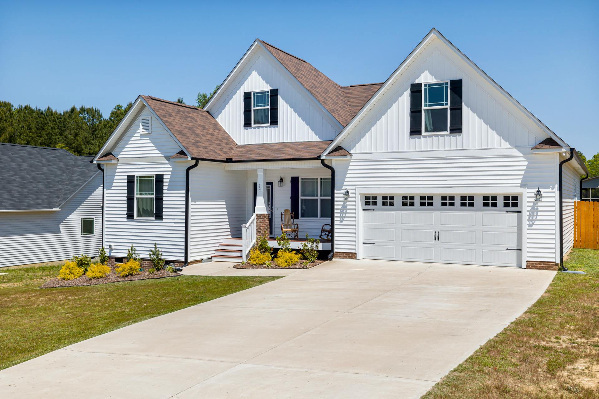 Newer two-storey home with white vinyl siding, dark shutters and a double garage