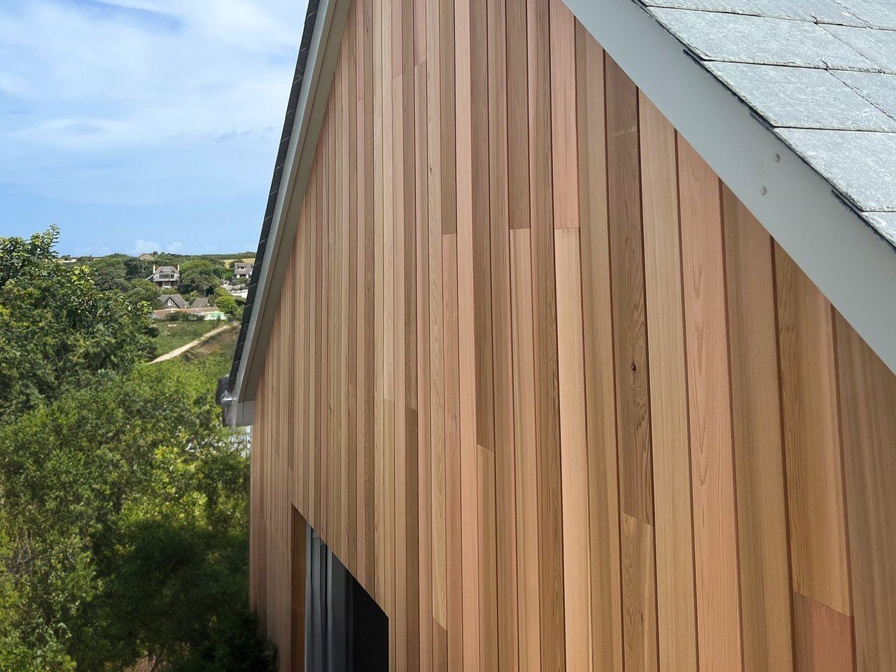 Vertical cedar-look cladding on a house gable with green foothills behind