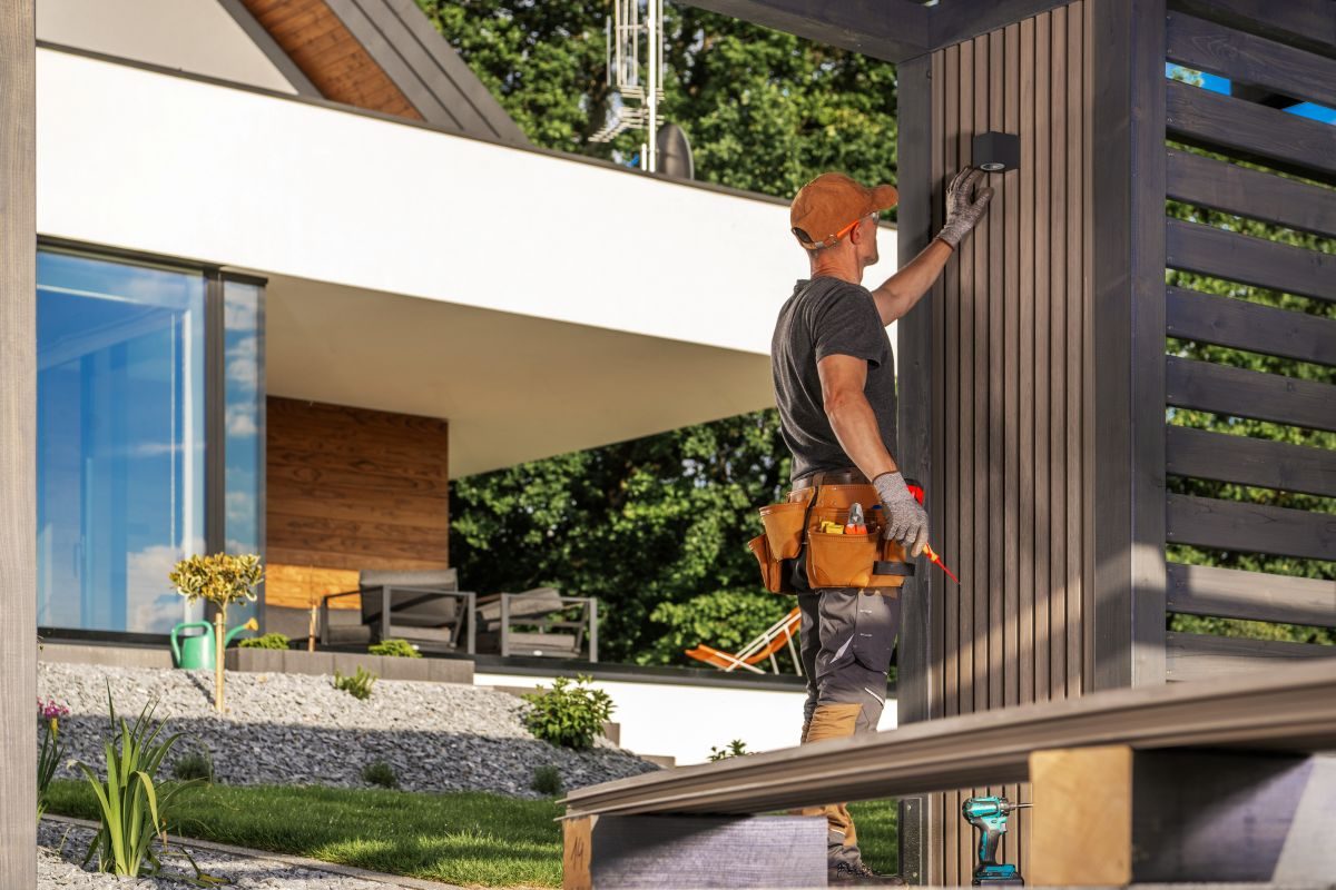 Painter finishing dark-stained wood siding on the exterior of a modern home