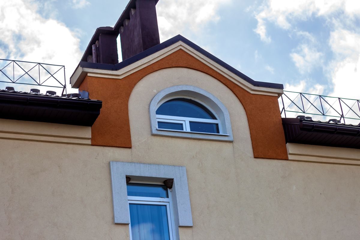 Cream stucco wall with an arched window and orange stucco accent band