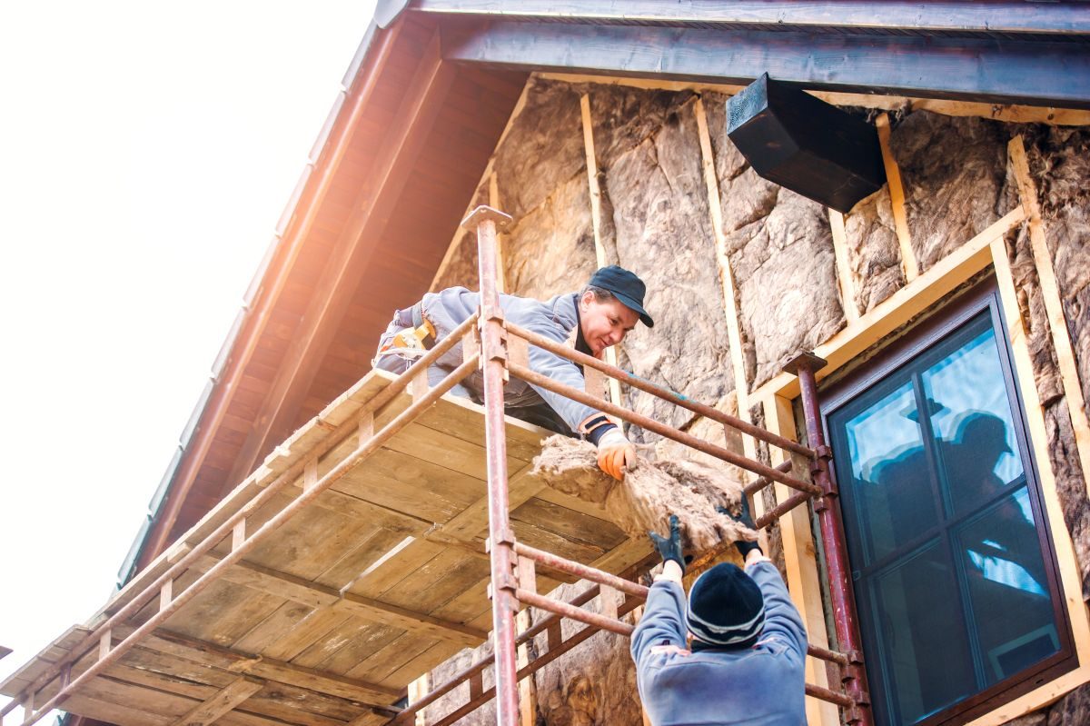 Crew working from scaffolding on the upper wall of a house beside a window