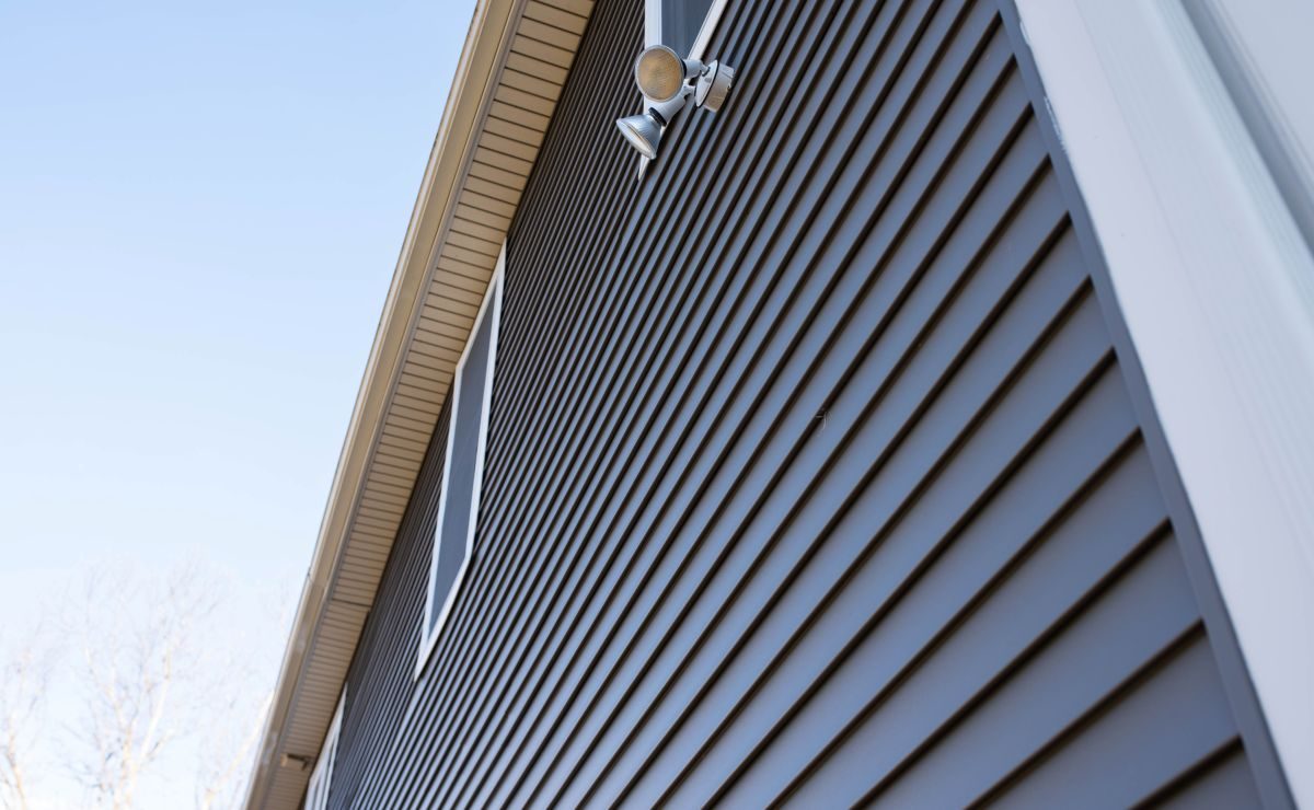 Dark grey vinyl siding on the upper wall of a home against a blue sky