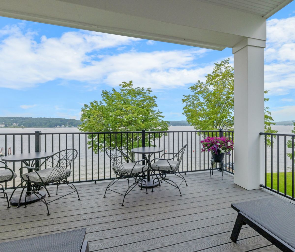 Covered grey composite deck with black aluminum railings and patio furniture overlooking a lake