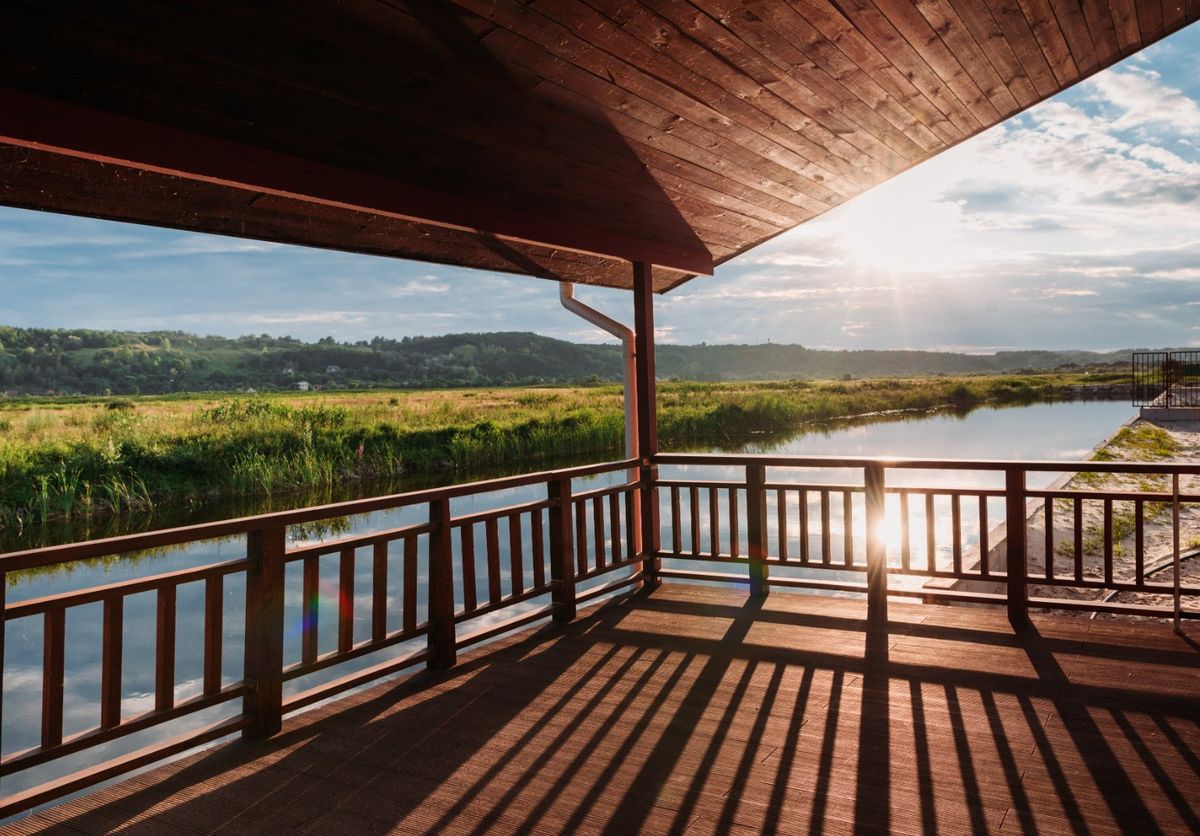 Covered wood deck with wood railings overlooking a river valley at sunset