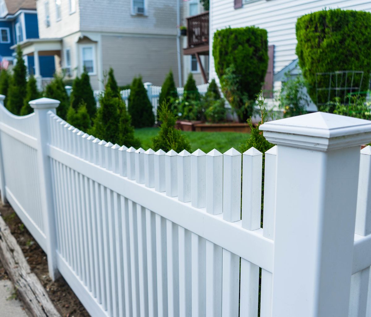 White vinyl picket fence with pyramid post caps along a residential sidewalk